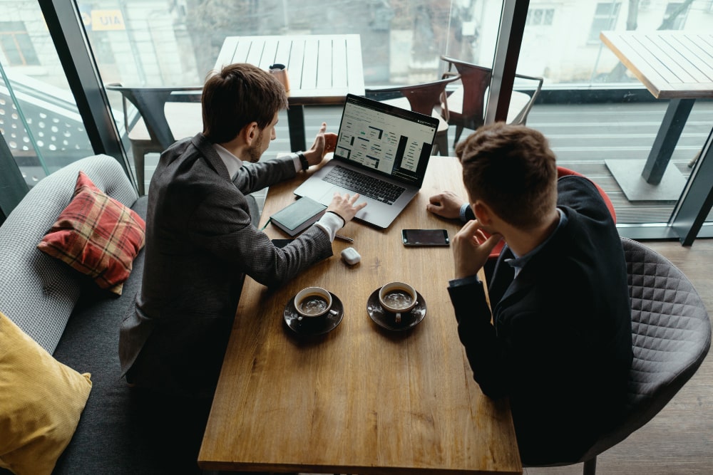 Two business consultants discussing data insights over laptops in a modern workspace, representing TalentIQ Ireland’s people-focused consulting services that solve challenges and drive sustainable growth.